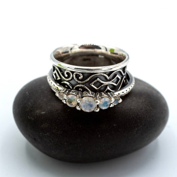 Silver ring with intricate design and gemstones on a black stone