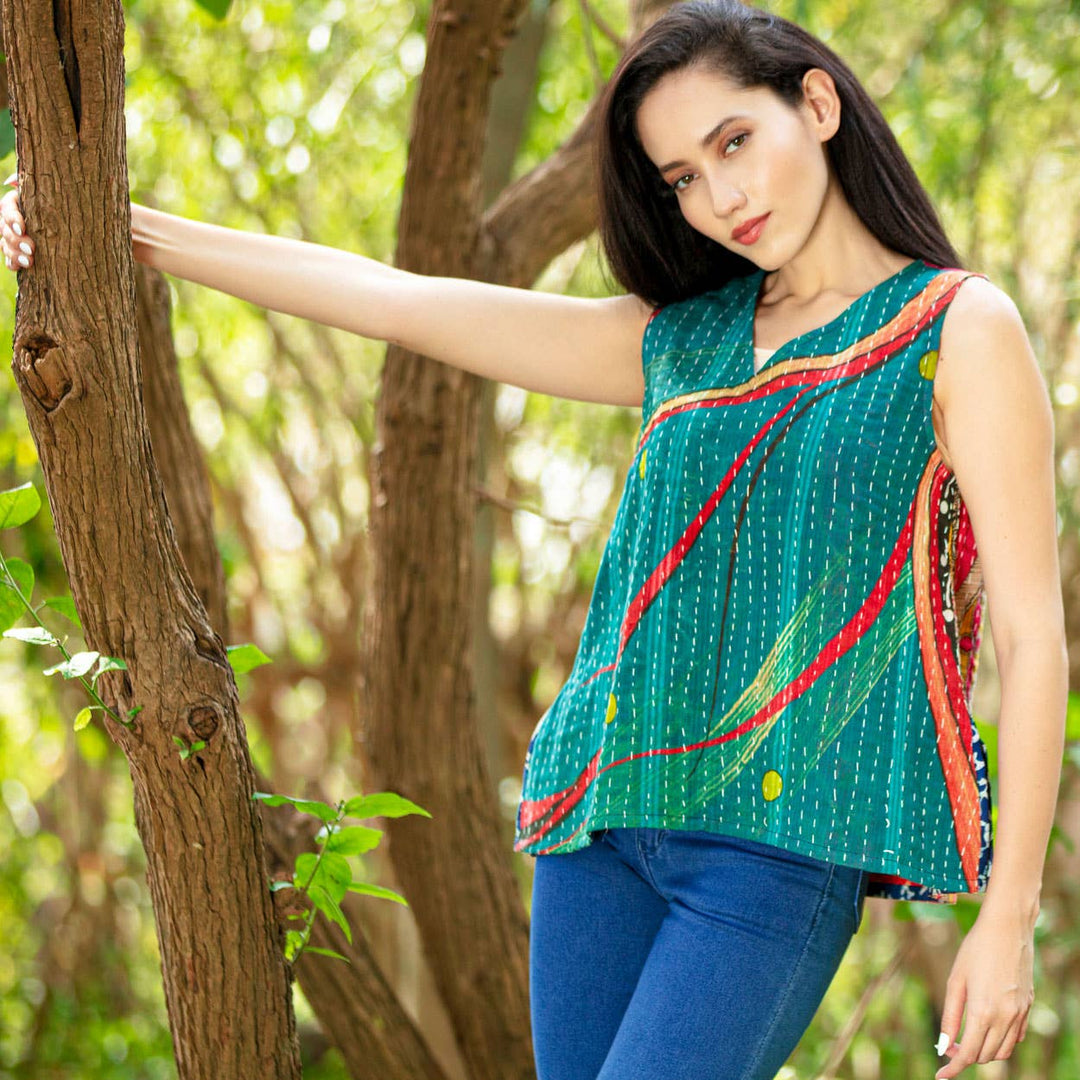 Woman wearing a colorful sleeveless top and blue jeans standing in a forest.