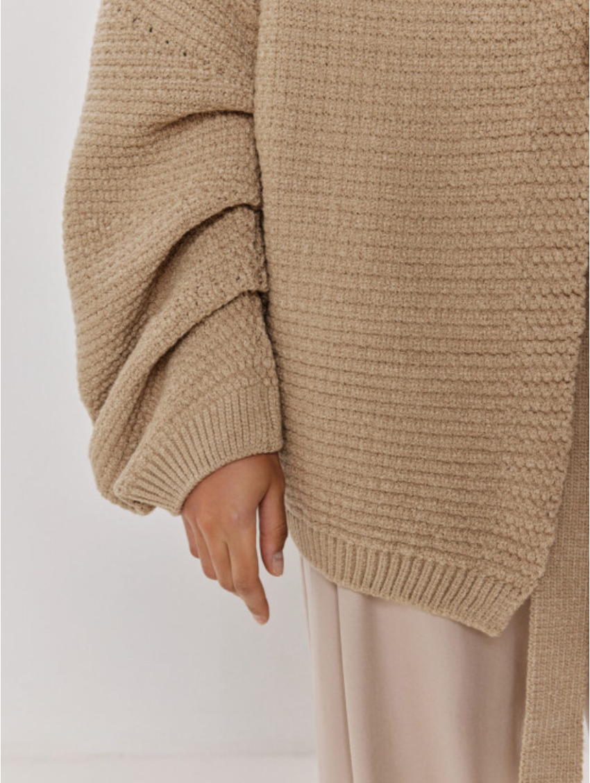 Beige knit sweater worn by a person on a plain background