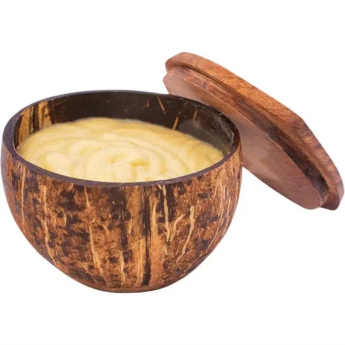 Coconut shell bowl with wooden lid containing a creamy substance on a white background