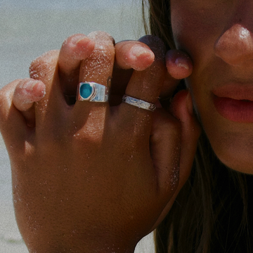 Close-up of a person's hands with rings on a beach.