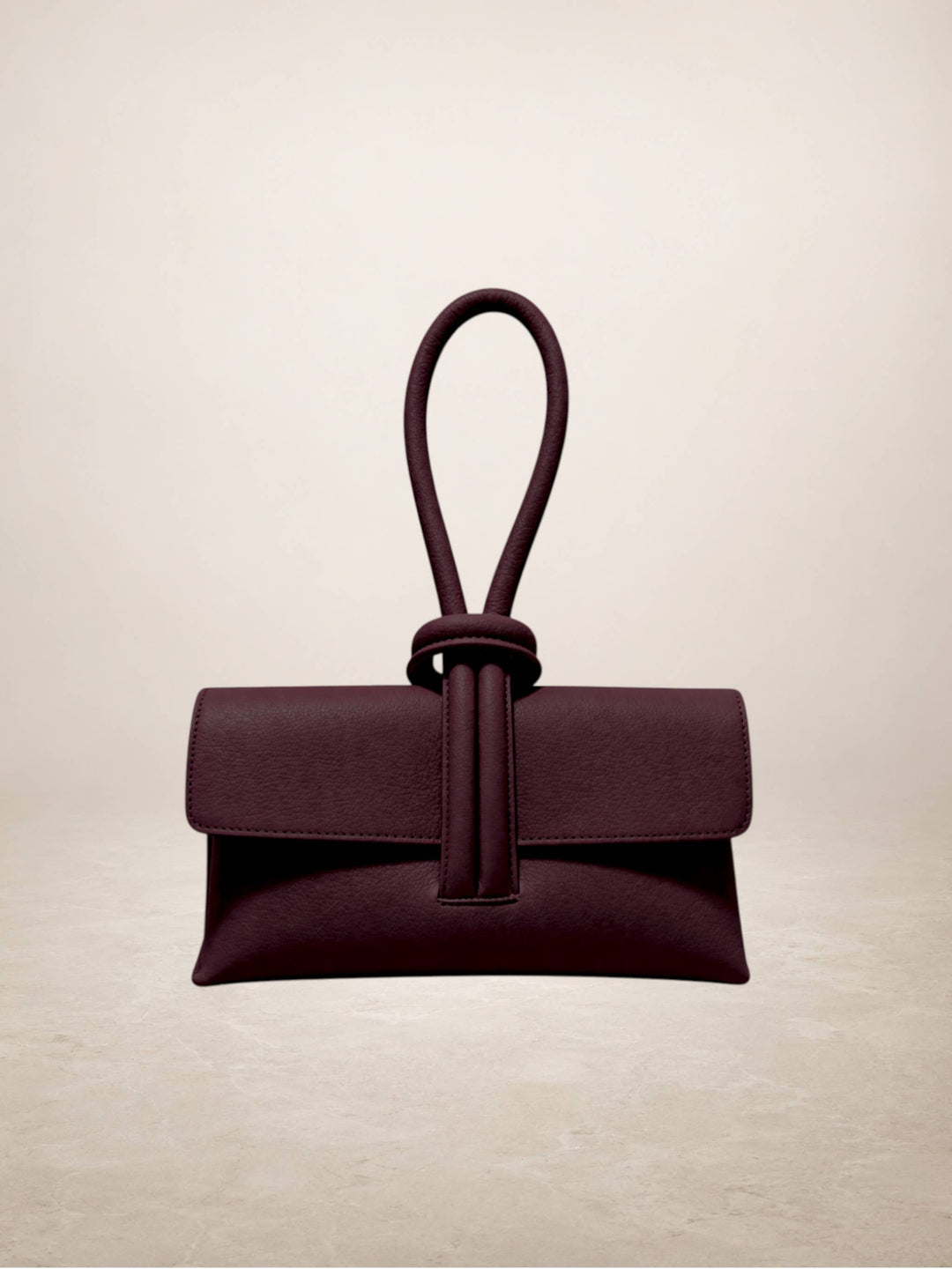 A dark plum purple leather clutch bag with a unique knotted top handle, displayed against a neutral beige background.