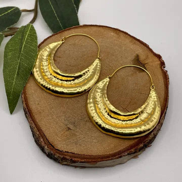 Gold hoop earrings on a wooden surface with leaves in the background