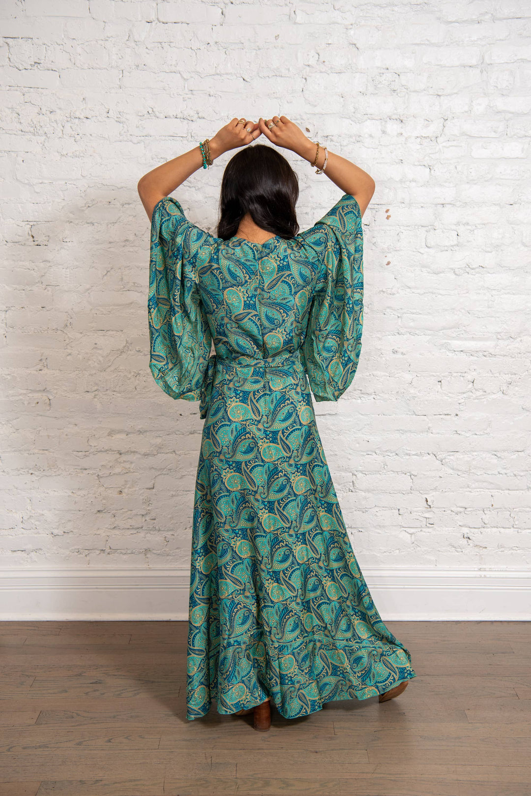 Woman wearing a green patterned dress standing against a white brick wall.