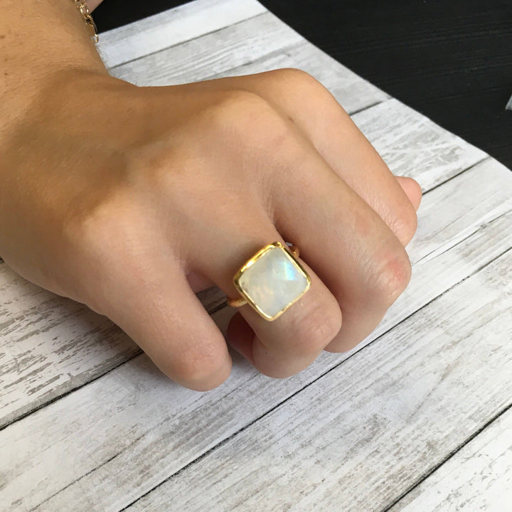 Hand wearing a gold ring with a large gemstone on a wooden surface