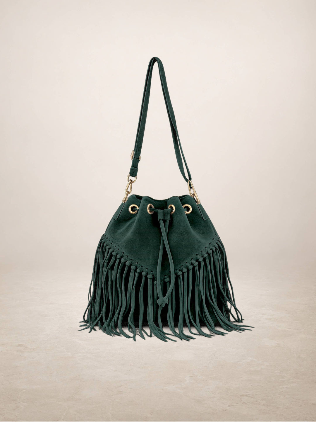 A dark green suede bucket bag with a long fringe detail, gold-tone hardware, and a matching shoulder strap, set against a neutral beige background.