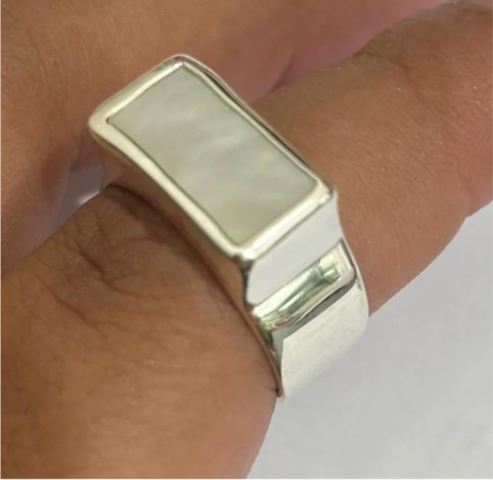 Silver ring with a rectangular stone on a finger against a neutral background