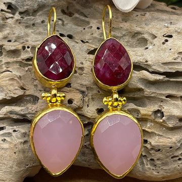 Gold earrings with red gemstones and pink teardrop-shaped stones on a wooden surface.