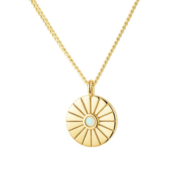 Gold necklace with a circular pendant featuring a central gemstone on a white background