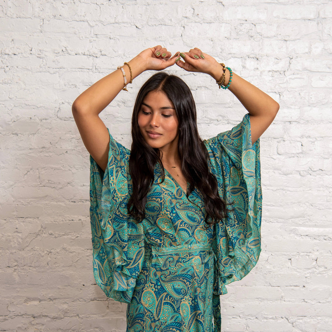 Woman wearing a green patterned outfit against a white brick wall