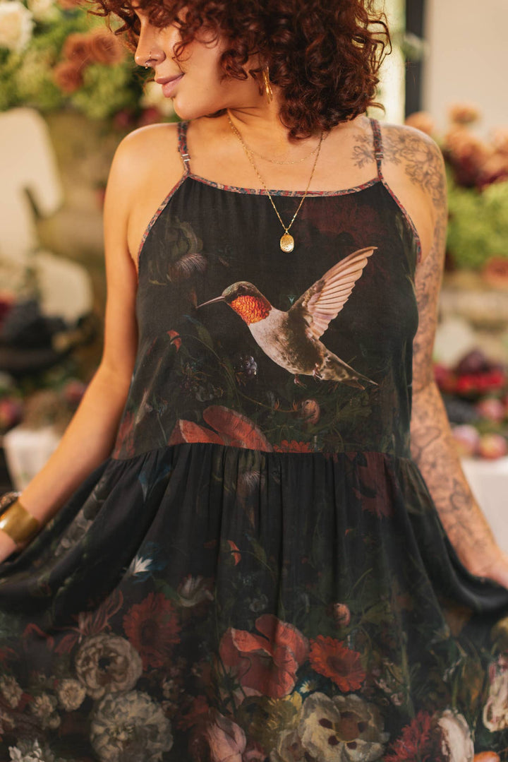 Woman wearing a black floral dress with a hummingbird design.