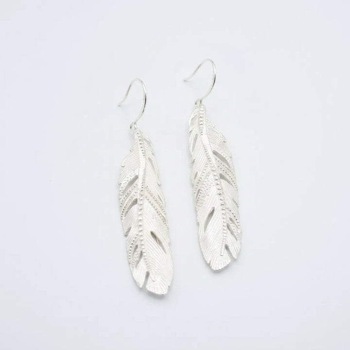 Silver feather-shaped earrings on a light gray background
